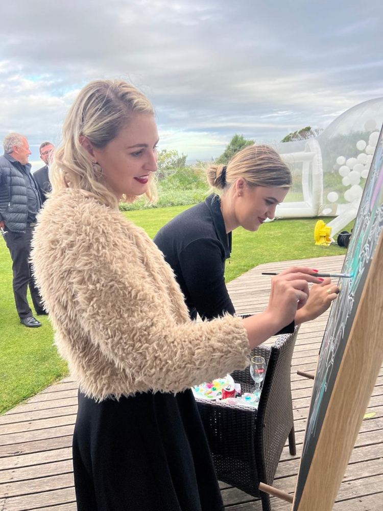 Guests painting at the easel on a deck with a sea view
