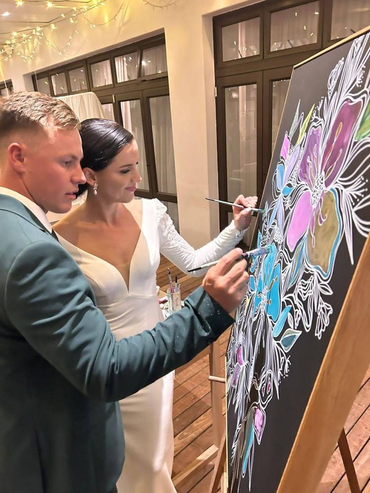 Bride and groom painting colour into a floral artwork at their reception