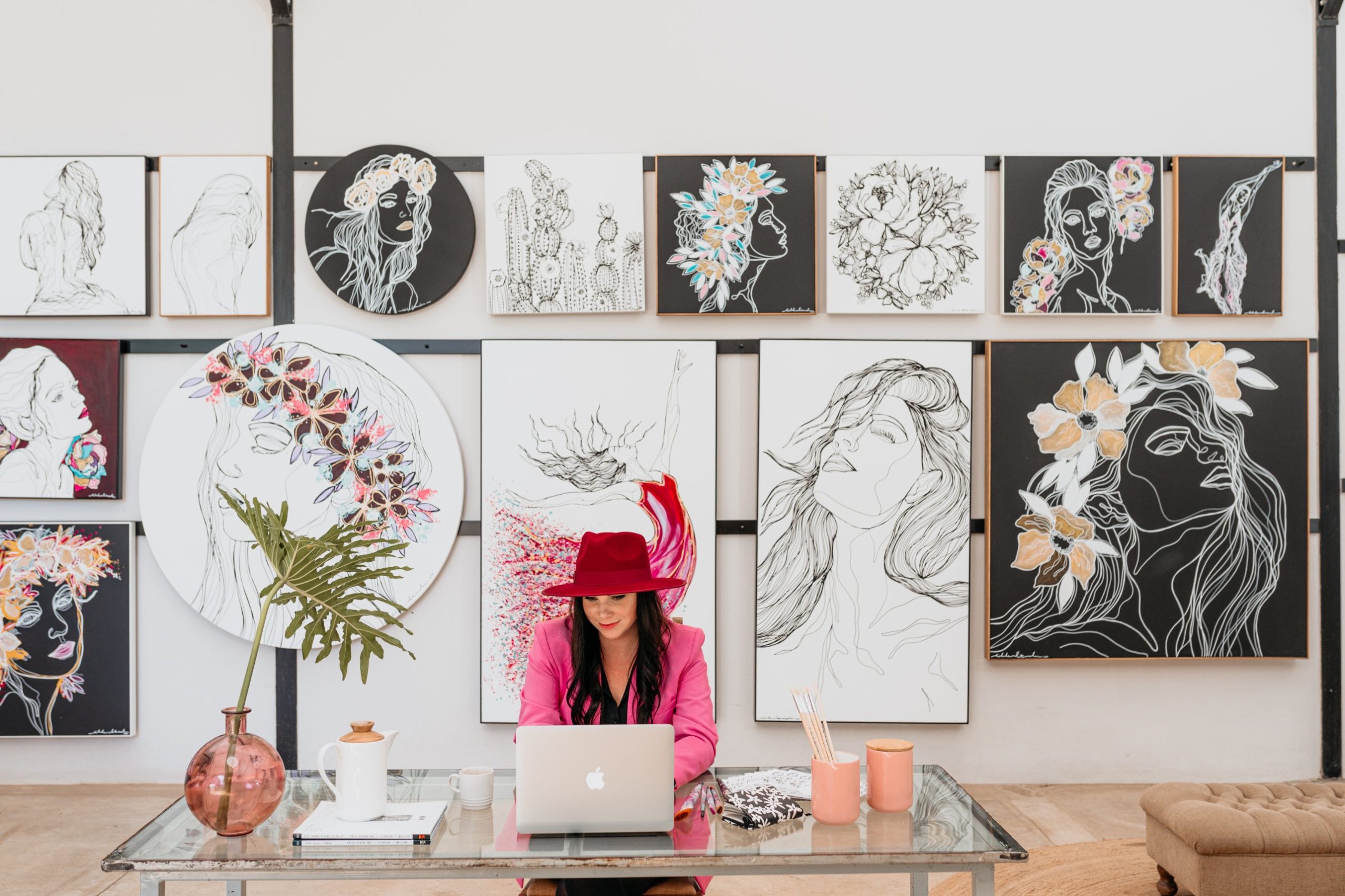 Hilde Alet Malan at her desk in front of a wall of her original artworks
